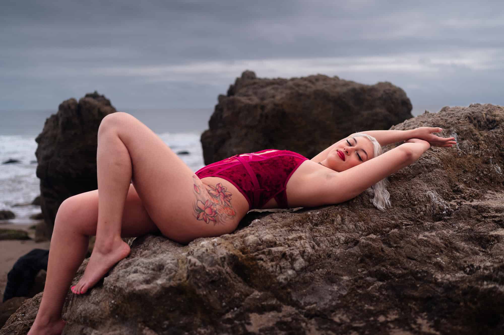 Lying Beach Boudoir photography in a red bodysuit on top of Rocks at El Matador in Los Angeles by Eli Boudoir