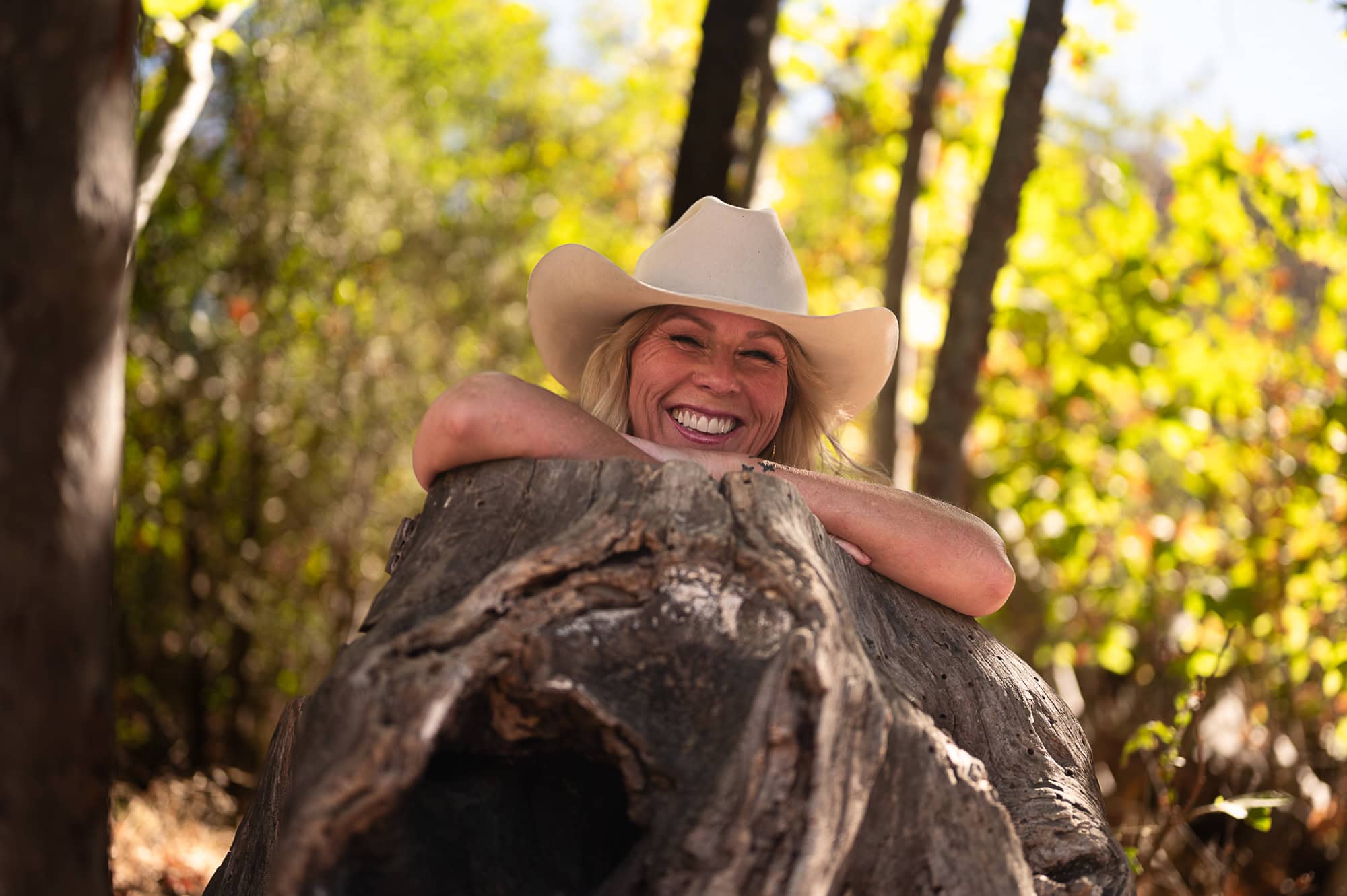 Wood outdoor boudoir photograph at Placeritas Canyon in Los Angeles with a Cowboy Hat leaning over a tree stump.