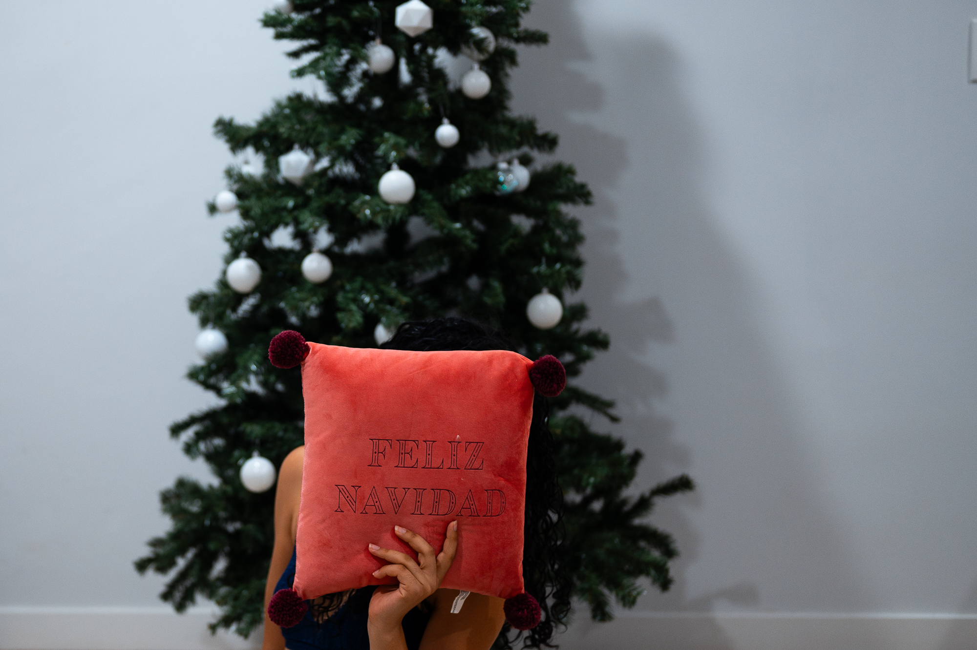 Decorating a Christmas Tree holding a Feliz Navidad pillow over my face