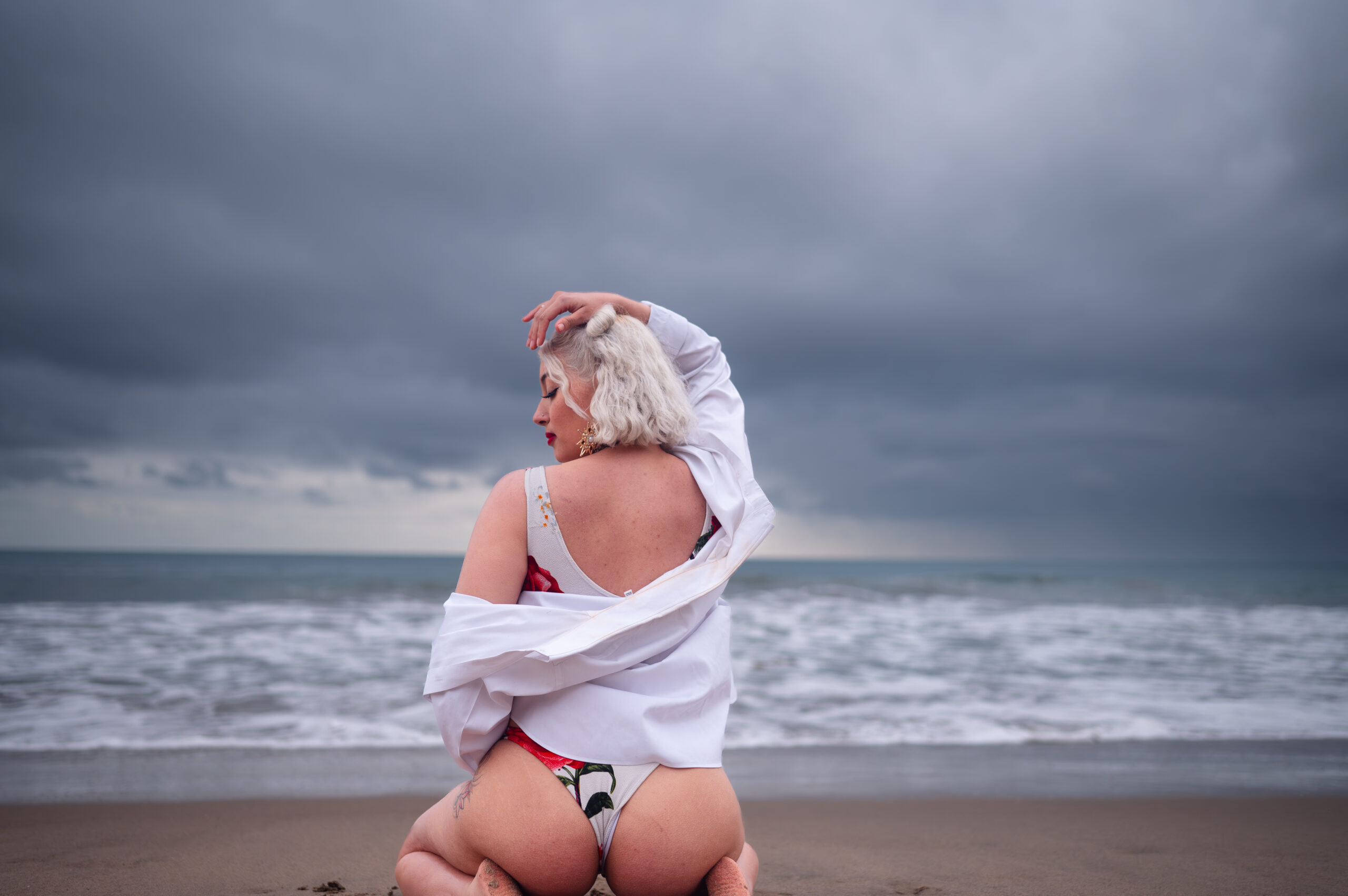boudoir photography client in Los Angeles sitting and looking over her shoulder during a Beach Boudoir photography in a white bikini with red roses at El Matador in Los Angeles by Eli Boudoir